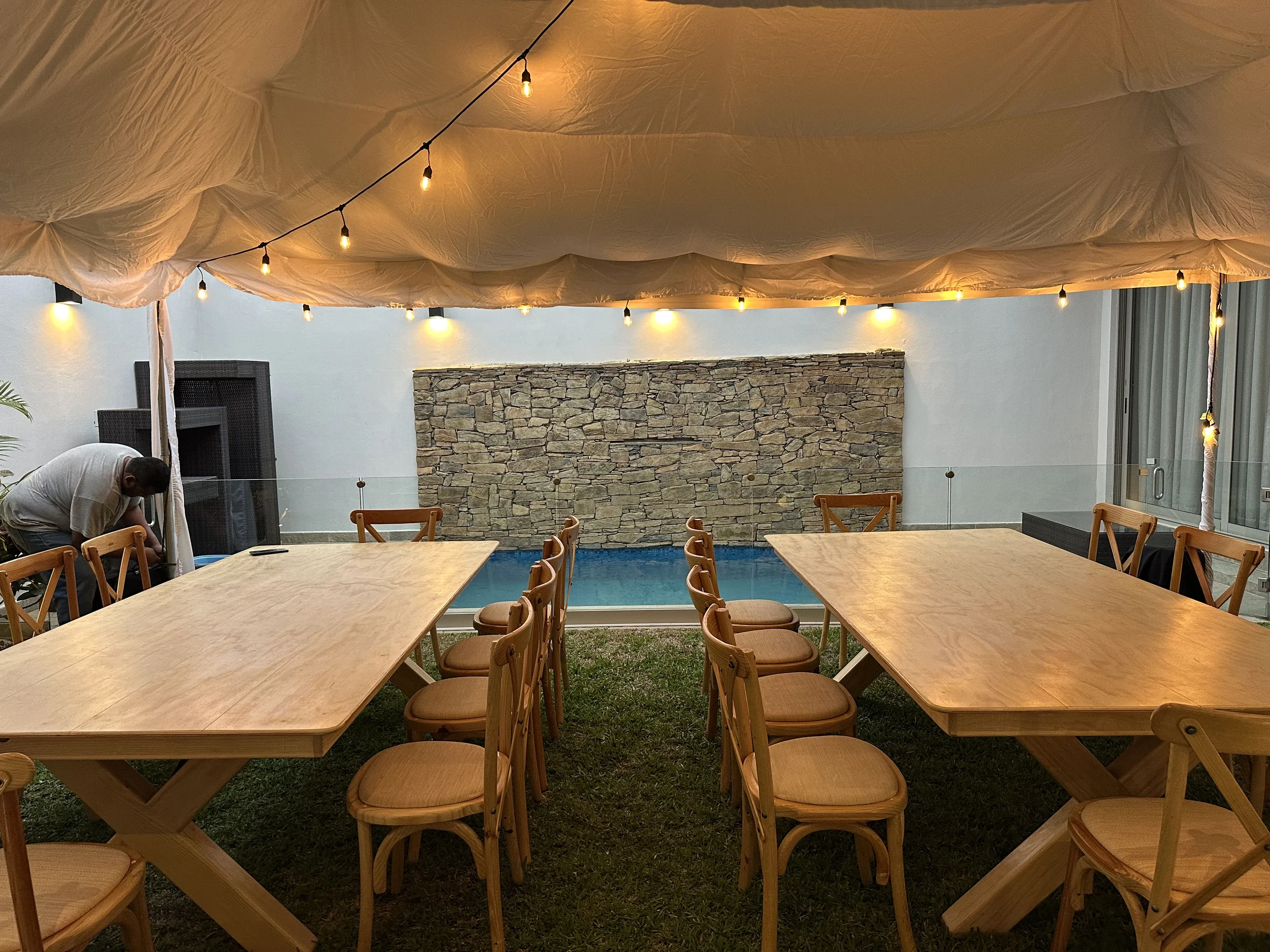 Toldo iluminado con mobiliario de madera junto a alberca